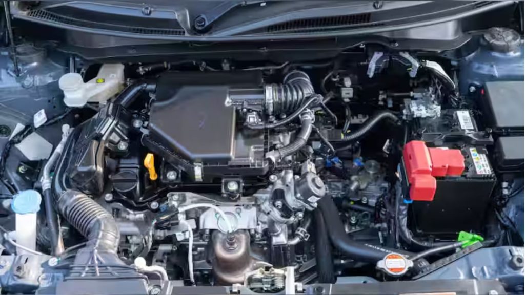 A detailed top-down photograph of the engine bay of the new Maruti Suzuki Dzire, revealing the Z-Series 1.2-litre 3-cylinder engine, battery, air intake, and fluid reservoirs.