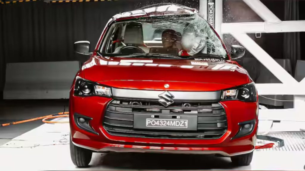 A dramatic front view capturing the Maruti Suzuki Dzire (PO4324MDZ1) during a crash test, showing structural deformation, airbag deployment, and shattered glass to illustrate its 5-star safety performance.