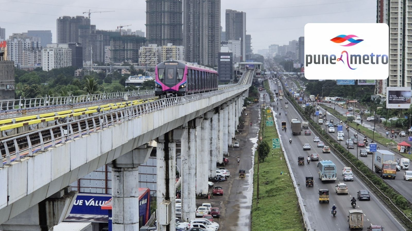 An aerial view photograph of an elevated Pune Metro Line 3 train, featuring its distinct pink and purple livery, travelling on a viaduct over a busy, rain-soaked city highway in the Pimpri-Chinchwad area, leading towards the Hinjawadi IT corridor. The image includes the official Pune Metro logo with its stylized blue and red weave. The photo illustrates the scale of the upcoming infrastructure project slated for a phased opening in May 2026.