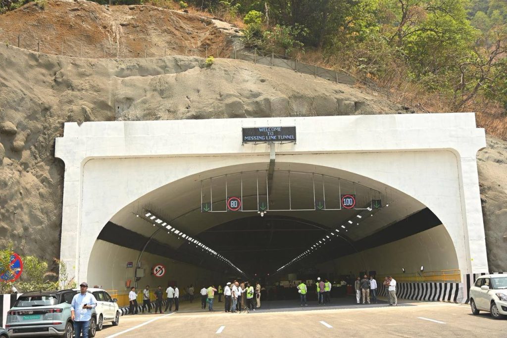 The bright, wide entrance of the "Missing Link" tunnel, featuring a white concrete portal with a "Welcome to Missing Link Tunnel" sign and overhead speed limit indicators of 80 and 100 kmph.
