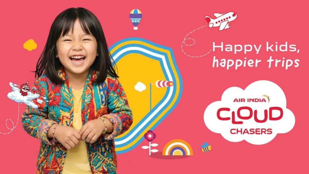 A young girl with dark hair and a colorful patterned jacket laughs joyfully against a vibrant pink background. To her right, the Air India Cloud Chasers logo is displayed inside a white cloud graphic, accompanied by the slogan "Happy kids, happier trips." The playful design includes whimsical illustrations of a cartoon airplane, a hot air balloon, a rainbow, and a reimagined, youthful version of the iconic Maharaja mascot flying on a small cloud.