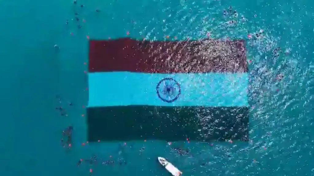 An aerial top-down view of the world's largest underwater Indian national flag floating in the turquoise waters of the Andaman Sea, surrounded by a team of divers and a support boat.