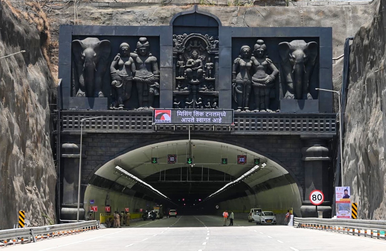 A wide-angle view showing the entrance of the Mumbai-Pune Expressway's Missing Link tunnel, framed by elaborate traditional stone-carved sculptures and an LED welcome sign in Marathi above the portal. Traffic signals and an 80 km/h speed limit sign are visible at the entrance.