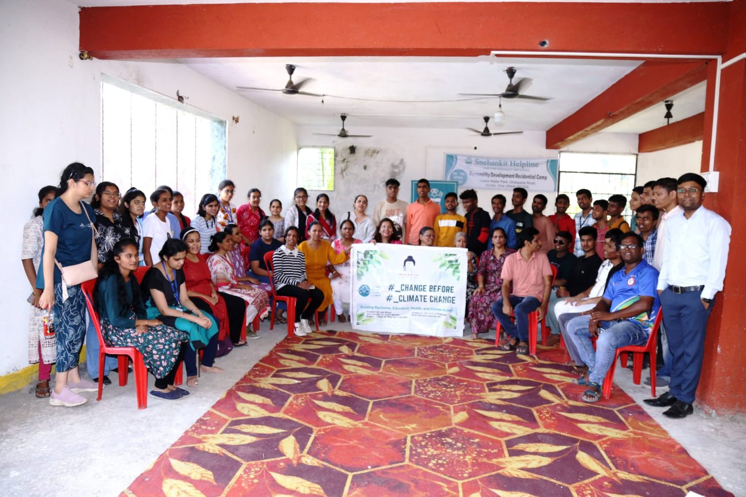 A large group of visually impaired students and organizers posing together at the Kalwa Resort in Virar. At the center, they hold a white banner that prominently reads "#_CHANGE BEFORE #_CLIMATE CHANGE," representing the environmental awareness component of the Tathaagat Foundation residential camp.