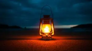A wide-angle photo of an oil lantern, lit and placed in dark spot in the evening with hills and dark night in the background.
