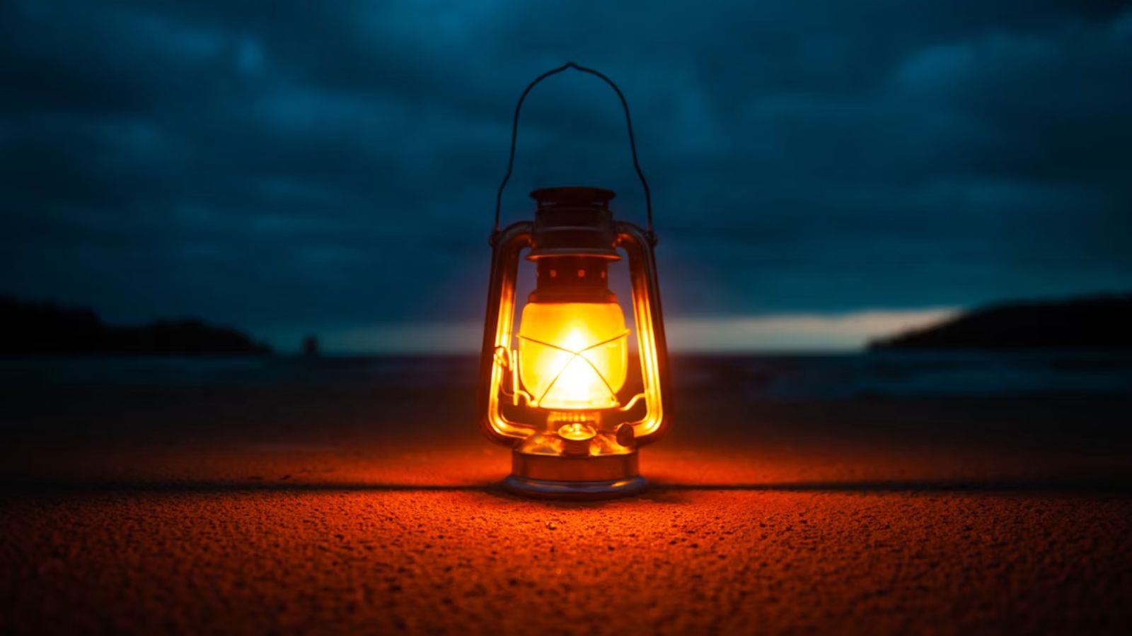 A wide-angle photo of an oil lantern, lit and placed in dark spot in the evening with hills and dark night in the background.
