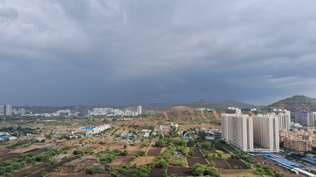 A wide-angle shot of Pune skyline, taken from a tall building. There are dark rain clouds gathering over city's skyline, including buildings and hills.