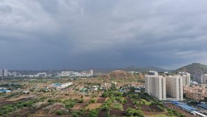 A wide-angle shot of Pune skyline, taken from a tall building. There are dark rain clouds gathering over city's skyline, including buildings and hills.