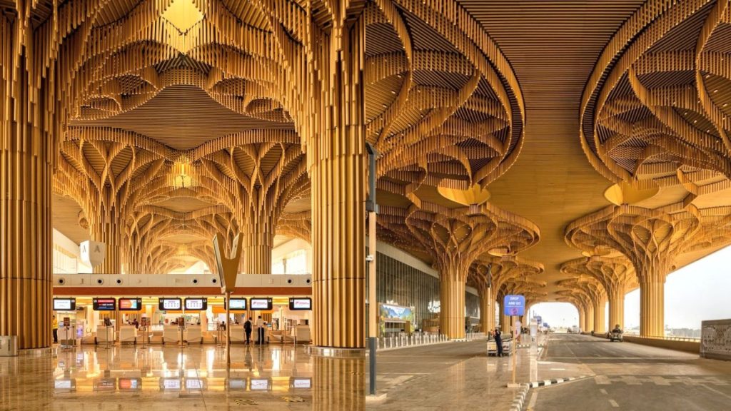 A two-panel side-by-side photograph showcasing the architecture of Terminal 2 at Lokpriya Gopinath Bordoloi International Airport in Guwahati. The left panel shows the interior check-in counter area with polished floors reflecting massive, tree-like vertical columns that branch out into intricate wooden latticework across the ceiling. The right panel shows the exterior passenger drop-off lane covered by an identical, expansive biophilic canopy structure supported by a row of matching, sculpted wooden pillars.